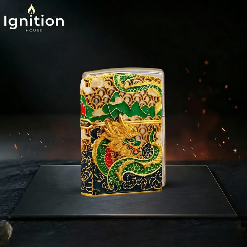 May include: A decorative metal lighter with a detailed dragon design in gold, green, and red. The lighter features the text "Ignition House" in white. The dragon is set against a backdrop of green mountains and a cream-colored sky.