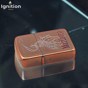 May include: A copper-colored metal lighter with the word "Marlboro" engraved on the top. The lighter has a detailed design of a horse and rider. The brand name "Ignition House" is in the top left corner.