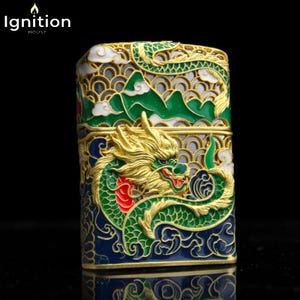 May include: A decorative lighter with a detailed dragon design. The lighter features a gold-colored dragon with green, red, and blue accents. The top of the lighter has a mountain and cloud design. The text "Ignition House" is in the upper left corner.