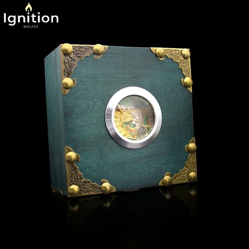 May include: A teal wooden box with brass corner accents and a circular window revealing a golden dragon figurine. The box has the text "Ignition House" in the upper left corner.