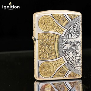 May include: A silver and gold lighter with intricate engraved designs. The lighter features a detailed illustration of a figure with scales, surrounded by ornate patterns and the text "Ignition House".