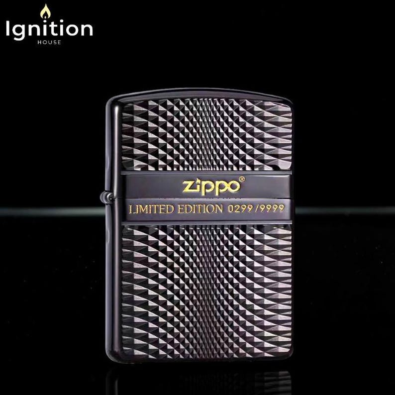 May include: Black Zippo lighter with a geometric pattern. The lighter has a black band with the Zippo logo in gold and the text "LIMITED EDITION 0299/9999". The lighter is a collectible item.