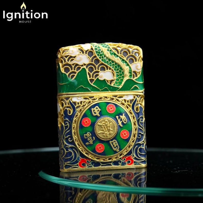 May include: An ornate, decorative lighter with a detailed design. The lighter features a green dragon, gold accents, and a blue and green circular emblem with Chinese characters. The top of the lighter has a green mountain design with white clouds.