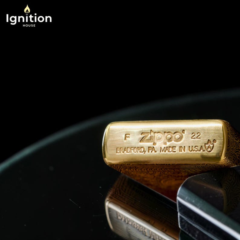 May include: Close-up of a gold-colored Zippo lighter with the text "Zippo 22" and "BRADFORD, PA. MADE IN U.S.A." The lighter has a textured pattern on the side and is set against a dark background.