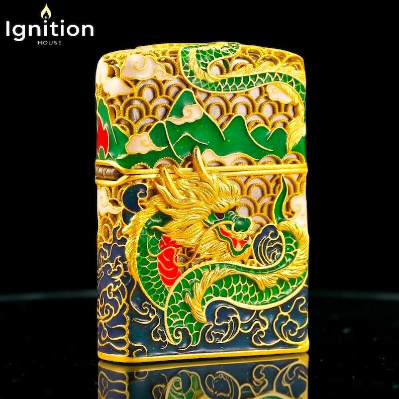 May include: Ornate gold-colored lighter with a detailed dragon design. The dragon is green and gold, set against a backdrop of green mountains and blue waves. The lighter has the text "Ignition House" in the upper left corner.