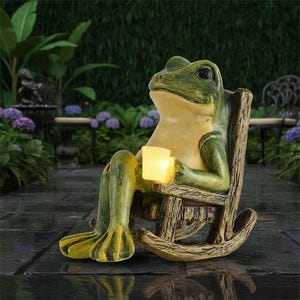 May include: A whimsical frog statue in a rocking chair, holding a glowing cube. The frog is green and yellow, with a relaxed expression. The chair is made of wood-like material. The scene is set outdoors, with a garden background.