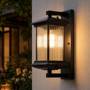 May include: A black rectangular outdoor wall light featuring a matte finish, a tiered top and bottom frame, and vertical ribbed glass panels. The fixture is mounted to a wall and emits a warm, glowing light from an internal bulb.