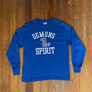 May include: A royal blue long-sleeve t-shirt with a white graphic of a cartoon devil holding a trident and the text "DEMONS SPIRIT" in a collegiate font.