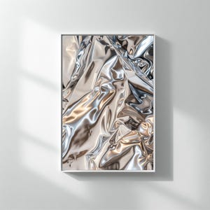 May include: A framed art print featuring a close-up of a shiny, metallic silver fabric. The fabric is heavily wrinkled, creating a dynamic play of light and shadow. The artwork is displayed in a white frame, adding a modern touch.