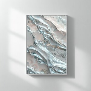 May include: Abstract art print in a white frame. The artwork features flowing, metallic silver and pale pink hues, creating a fluid, textured appearance. The piece is mounted on a white wall, with shadows adding depth.