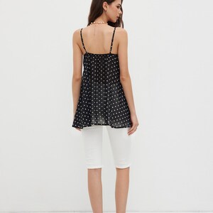 K&ouml;nnte beinhalten: Ein schwarzes Camisole-Top mit wei&szlig;en Punkten und Spaghettitr&auml;gern, kombiniert mit wei&szlig;en Caprihosen. Die Person tr&auml;gt schwarz-wei&szlig; gepunktete Abs&auml;tze.