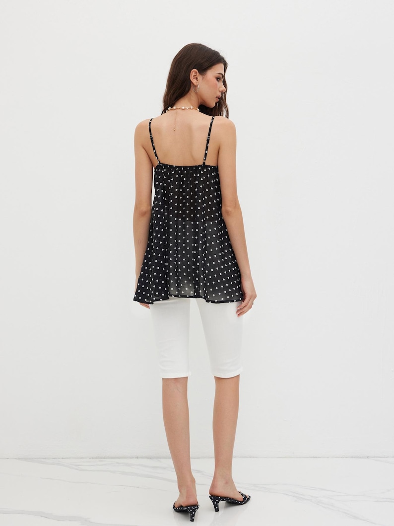 K&ouml;nnte beinhalten: Ein schwarzes Camisole-Top mit wei&szlig;en Punkten und Spaghettitr&auml;gern, kombiniert mit wei&szlig;en Caprihosen. Die Person tr&auml;gt schwarz-wei&szlig; gepunktete Abs&auml;tze.