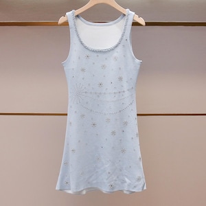 Puede incluir: Vestido sin mangas azul claro con cuello redondo, adornado con brillantes adornos. El vestido presenta un diseño decorativo de estrellas y líneas, colgado de una percha de madera.