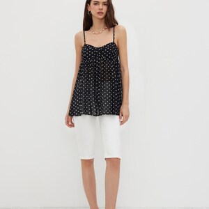 K&ouml;nnte beinhalten: Eine Frau tr&auml;gt ein schwarzes Polka-Dot-Camisole-Top mit d&uuml;nnen Tr&auml;gern und wei&szlig;e Shorts. Das Camisole hat einen Sweetheart-Ausschnitt. Sie tr&auml;gt au&szlig;erdem eine Perlenkette und schwarze Polka-Dot-Abs&auml;tze.