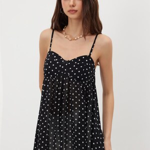 K&ouml;nnte beinhalten: Ein schwarzes Camisole-Top mit wei&szlig;en Polka-Dots. Das Top hat d&uuml;nne Spaghettitr&auml;ger und einen Sweetheart-Ausschnitt. Der Stoff wirkt leicht und flie&szlig;end. Ein stilvolles Kleidungsst&uuml;ck.