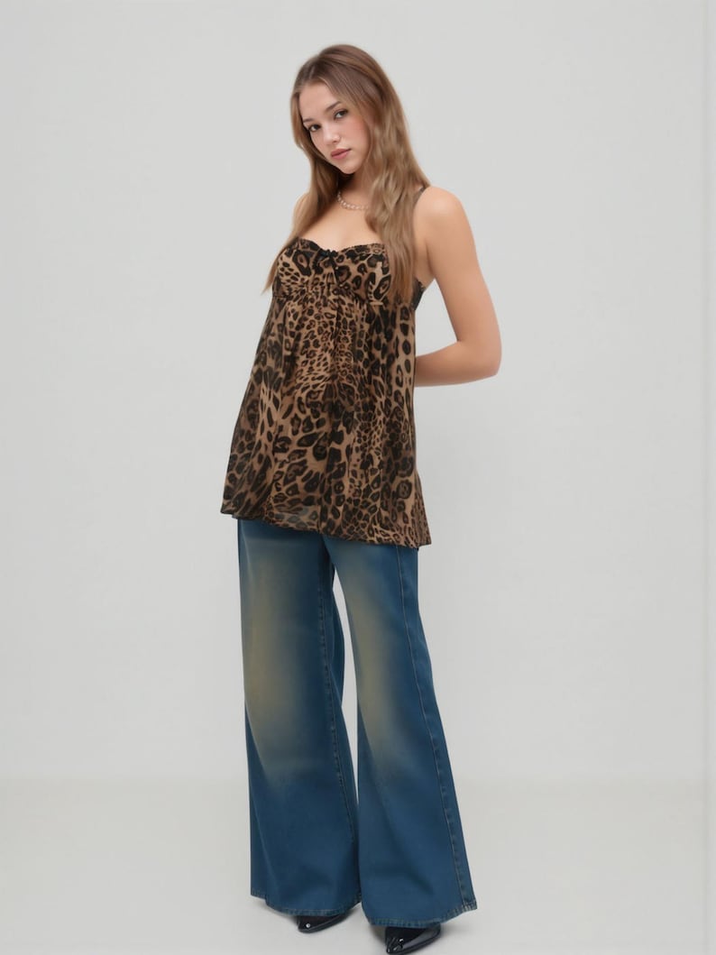 K&ouml;nnte beinhalten: Ein Outfit f&uuml;r Damen mit einem Oberteil mit Leopardenmuster und einer Jeans mit weitem Bein in Blau. Das Oberteil hat einen Sweetheart-Ausschnitt und d&uuml;nne Tr&auml;ger. Die Jeans hat eine verwaschene Optik und eine ausgestellte Silhouette. Das Outfit ist l&auml;ssig und modisch.