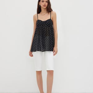 K&ouml;nnte beinhalten: Eine Frau tr&auml;gt ein schwarzes Polka-Dot-Camisole-Top mit d&uuml;nnen Tr&auml;gern und wei&szlig;e Shorts. Das Camisole hat einen Sweetheart-Ausschnitt. Sie tr&auml;gt au&szlig;erdem eine Perlenkette und schwarze Polka-Dot-Abs&auml;tze.