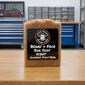 Pu&ograve; includere: Una saponetta marrone con un'etichetta nera che recita "BEARD + FACE BAR SOAP SCENT Guinness Stout Beer". Il sapone &egrave; confezionato in plastica trasparente. Lo sfondo comprende armadi e attrezzi blu.