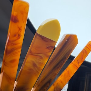 Op de afbeelding: Close-up van verschillende amberkleurige, rechthoekige objecten met een gemarmerd patroon. Eén object heeft een gele punt. De objecten zijn in verschillende hoeken gerangschikt, waardoor een dynamische compositie ontstaat. De achtergrond is een lichtblauwe lucht.