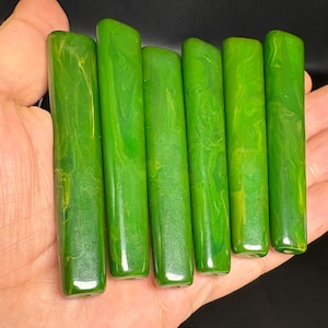 Puede incluir: Seis cuentas rectangulares y alargadas con un acabado liso y pulido. Cada cuenta presenta un color verde vibrante con patrones marmolados y arremolinados en tonos más claros de verde amarillento y lima, creando un aspecto orgánico.