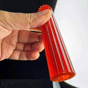 Könnte beinhalten: Ein durchscheinendes, leuchtend orangefarbenes zylindrisches Objekt mit einer tief geriffelten oder gerippten Außenstruktur. Der Gegenstand ist hohl, mit einer kreisförmigen Öffnung an der Basis, und weist eine durchgehend gleichmäßige, helle, halbtransparente orange Farbe auf.