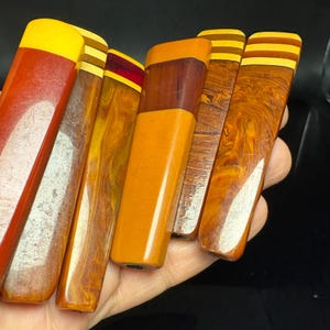 May include: A collection of six rectangular, elongated resin accessories featuring a mix of solid yellow, deep orange, and marbled brown patterns. Some pieces include horizontal yellow stripes or solid yellow caps, while others display a smooth, polished finish with swirling amber-toned textures.