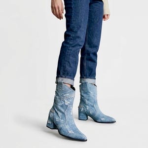 Könnte beinhalten: Hellblaue Denim-Stiefeletten mit abgenutzter, ausgefranster Textur und spitzer Zehenpartie. Die Stiefel verfügen über einen Blockabsatz, sichtbare Nähte und eine vom Western-Stil inspirierte Silhouette, kombiniert mit dunkelblauen Jeans mit Umschlag.