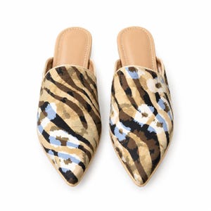 May include: A pair of pointed-toe mules featuring a tan, brown, and black animal-inspired print with light blue circular accents. The slip-on shoes have a beige interior lining and a low-profile design with a clean, structured silhouette.