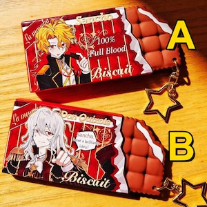 Può includere: Due portachiavi a forma di biscotto, rossi e marroni. Uno presenta un personaggio anime biondo con la scritta "Sancho 100% Full Blood Biscuit." L'altro mostra un personaggio anime dai capelli bianchi con la scritta "Don Quixote Biscuit."