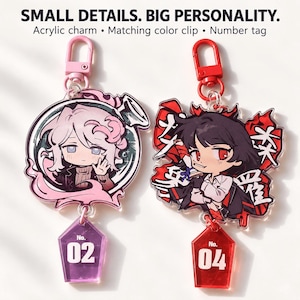 May include: Two acrylic charms with matching clips and number tags. The left charm features a character with pink hair in a circular frame with a purple tag labelled No. 02. The right charm shows a character with black hair and red eyes with a red tag labelled No. 04. Text reads: SMALL DETAILS. BIG PERSONALITY. Acrylic charm • Matching colour clip • Number tag.