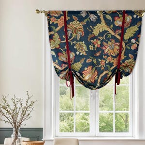 May include: A navy blue window valance with a floral pattern in shades of orange, green, and gold. The valance is tied up with red ribbons and hangs above a white window. The window looks out onto a green, leafy landscape.