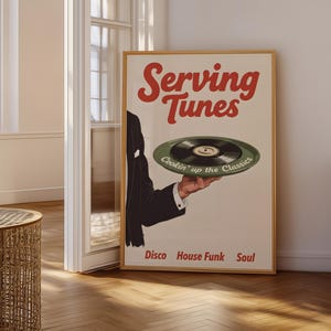Op de afbeelding: Een ingelijste poster met de rode woorden "Serving Tunes", met een hand die een groene vinylplaat vasthoudt. De poster bevat ook de woorden "Disco House Funk Soul" in een retro-stijl.