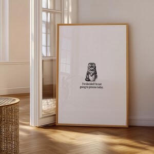 May include: A framed print with a black and white illustration of a cat holding a mug. The text below the image reads, "I've decided I'm not going to process today." The artwork is displayed in a light-coloured wooden frame.