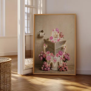 May include: A framed artwork depicts a surreal scene of a toilet overflowing with pink roses. The toilet is positioned in a bathroom setting, with a roll of toilet paper visible. The artwork has a vintage aesthetic.