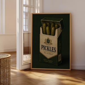 May include: A framed wall art print featuring a rectangular box designed like a cigarette pack, filled with five green pickles instead of cigarettes. The box is labelled PICKLES DILL & GARLIC with a crest logo and text reading ZESTY CRUNCHY ALWAYS FRESH.
