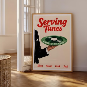 May include: A framed poster with the words "Serving Tunes" in red. A hand in a black suit holds a green vinyl record. Below the record are the words "Disco House Funk Soul". The poster is in a room with a wooden floor.