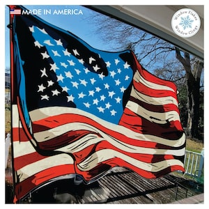 May include: A window cling featuring a stylized American flag design. The flag is depicted with bold red and white stripes and a blue field of white stars. The words "MADE IN AMERICA" are printed at the top. The product is from "Window Flakes Window Clings".