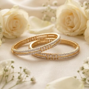 May include: Two gold bangles featuring a double row of small round stones and a central section of baguette-cut stones. The bracelets have a polished metallic finish and are arranged in an overlapping position, showcasing a detailed channel setting.