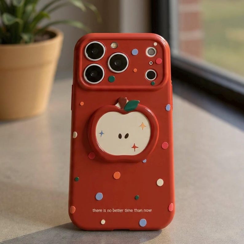 May include: Red phone case with an apple design and colorful polka dots. The case has a cutout for the camera and the text "there is no better time than now".
