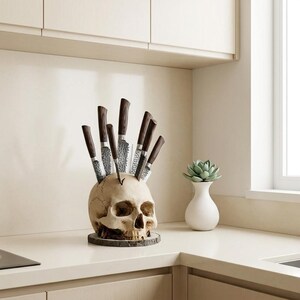 May include: A beige skull-shaped knife holder with multiple knives inserted, creating a unique kitchen decor piece. The knives have dark brown handles and silver blades. The holder sits on a wooden base, adding a rustic touch.