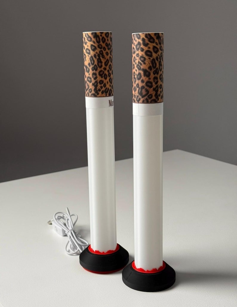 May include: Two white cylindrical lamps with a leopard print top and a black base with a red accent. The lamps are plugged in with a white cord. The text "Ma" is visible on the lamps.