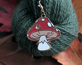 May include: A red and white mushroom shaped stitch marker with a gold metal loop. The marker is on a green ball of yarn.