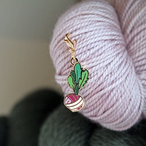 May include: A gold-coloured metal charm in the shape of a turnip with green leaves. The charm is attached to a gold-coloured chain.