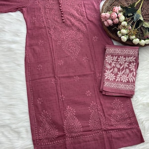 K&ouml;nnte beinhalten: Staubrosa besticktes Tunika- und passendes Schal-Set. Die Tunika hat detaillierte Blumenstickereien und kleine Knopfverschl&uuml;sse. Der Schal hat ein florales Bord&uuml;rendesign. Das Set wird auf einem Holzb&uuml;gel pr&auml;sentiert.