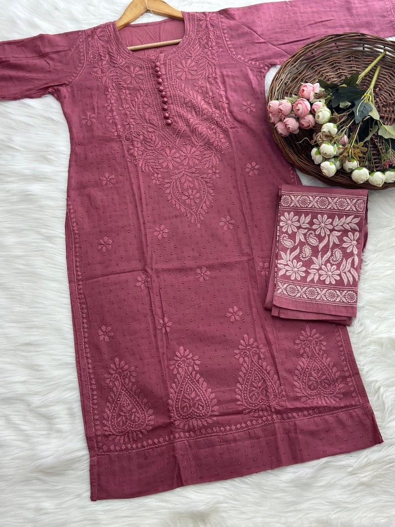 K&ouml;nnte beinhalten: Staubrosa besticktes Tunika- und passendes Schal-Set. Die Tunika hat detaillierte Blumenstickereien und kleine Knopfverschl&uuml;sse. Der Schal hat ein florales Bord&uuml;rendesign. Das Set wird auf einem Holzb&uuml;gel pr&auml;sentiert.