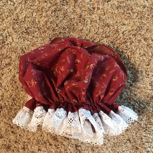 May include: A red fabric shower cap with a white lace trim. The cap has a floral pattern.