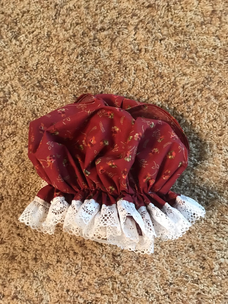 May include: A red fabric shower cap with a white lace trim. The cap has a floral pattern.