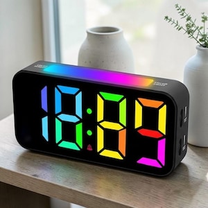 May include: Black digital alarm clock with a rainbow LED display showing the time. The clock has a rectangular shape with rounded corners and two USB ports. The display shows the time in large, colorful digits.