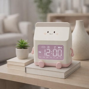 May include: A white and pink digital alarm clock shaped like a milk carton, with a smiling face and small arms and legs. The clock displays the time as 12:00 PM. The clock is sitting on a stack of books.