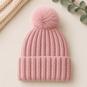 Pu&ograve; includere: Un berretto rosa polvere caratterizzato da una spessa trama a maglia a coste e un ampio risvolto ripiegato. Il cappello &egrave; sormontato da un grande pon-pon soffice coordinato. Il design presenta un motivo a maglia verticale su tutta la calotta.